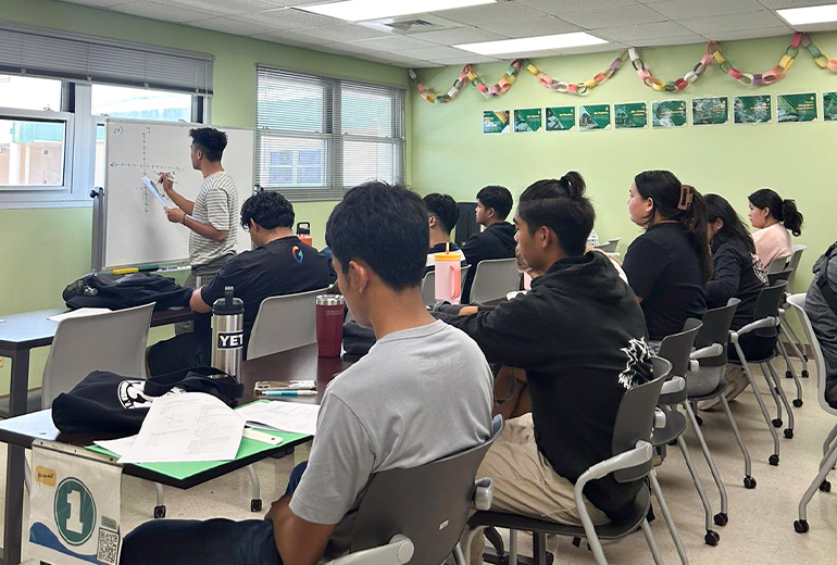 Tutor speaks and writes on board in front of full classroom of Triton Summer Academy students
