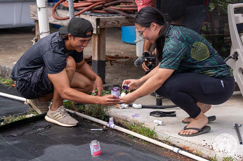 Two people applying glue to a PVC pipe