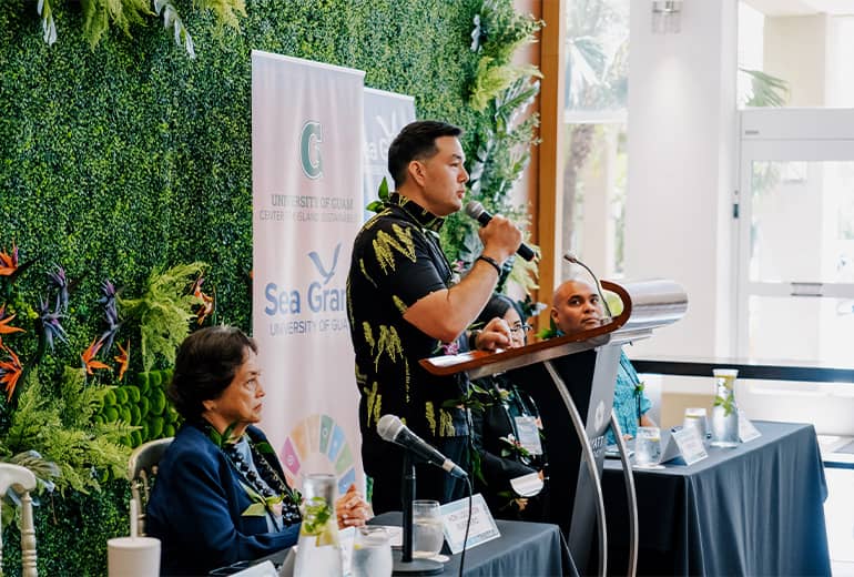 Austin Shelton speaks at podium next to Guam Governor Lou Leon Guerrero at CIS and Sea Grant event at Hyatt Regency Guam
