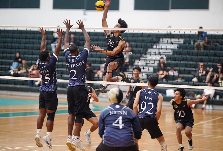 Players on one side of volleyball net block a spike from opposing team