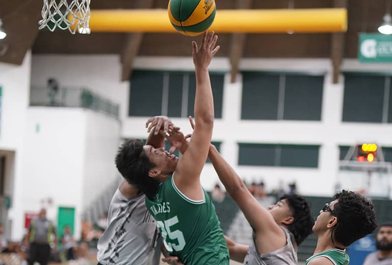 players in white jerseys try to block player in green jersey's basketball shot