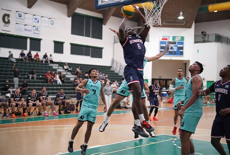 Basketball player in dark blue jersey goes for dunk shot with opponents surrounding