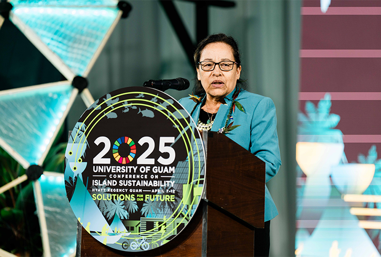 Hilda Heine speaks at podium with 2025 UOG CIS poster/logo on the front