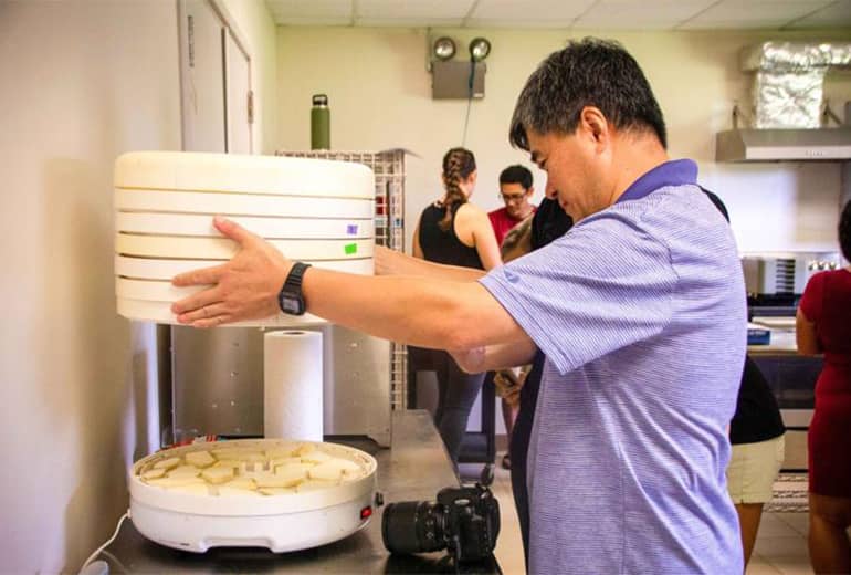 Man holds up piece of dehydrator over cookies to go through